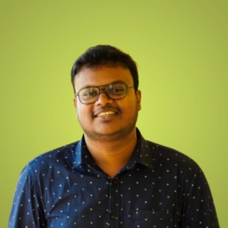 Freelance digital marketing expert in Kottayam wearing glasses and a navy blue shirt against a green background.